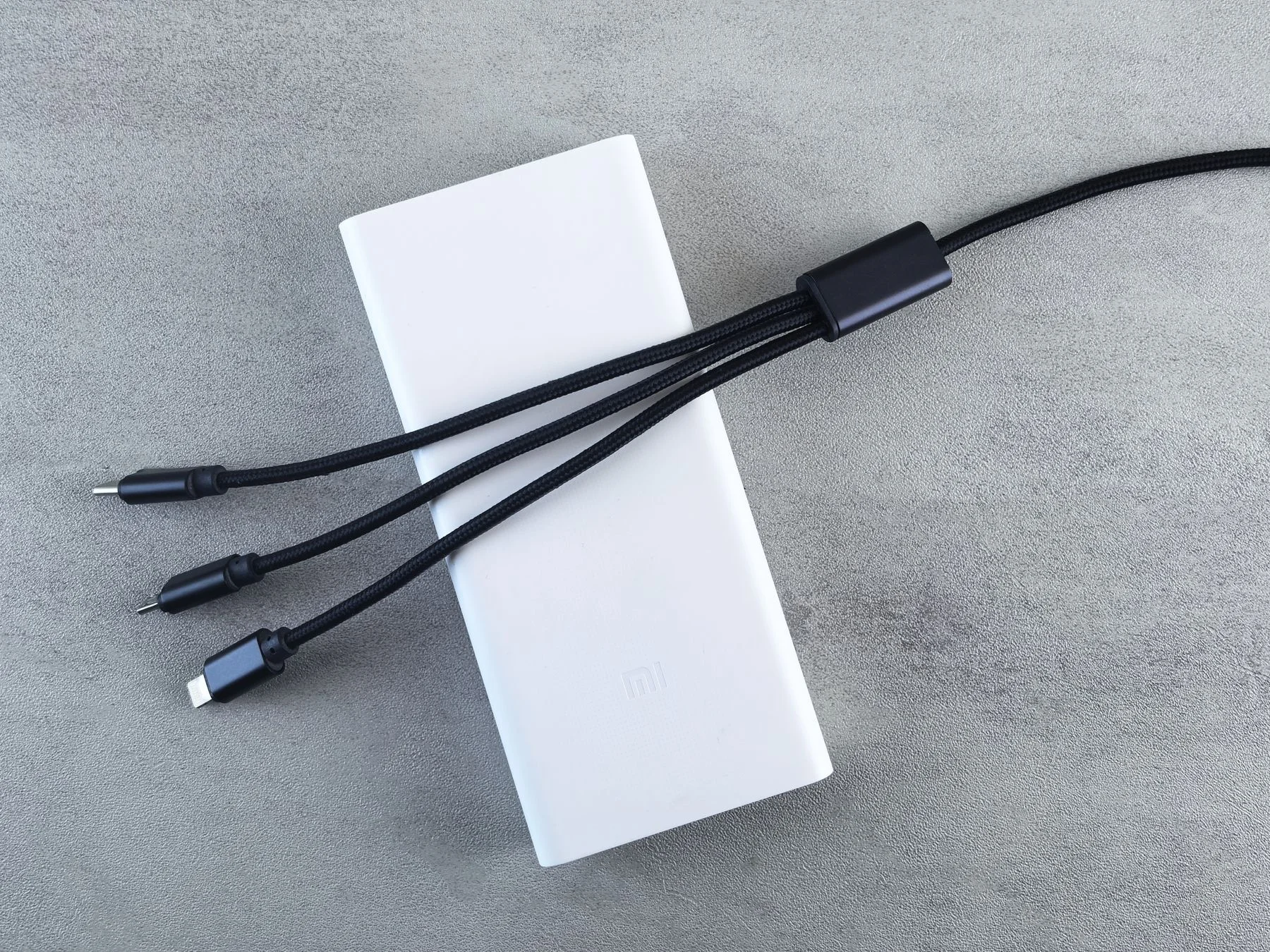 A white portable power bank and a black charging cable on a grey surface