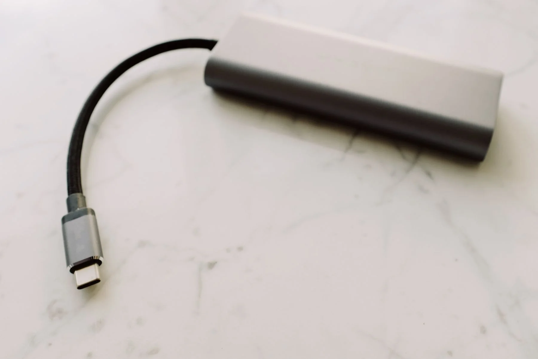A silver USB-C hub with its attached connector on a marble surface